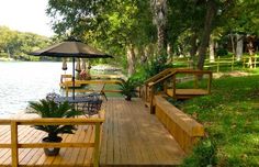 a wooden deck with chairs and an umbrella on it next to the water in a park