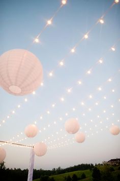 white paper lanterns are strung from the ceiling above an outdoor wedding ceremony area at dusk