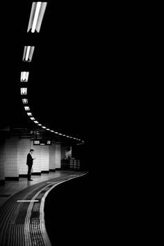 black and white photograph of a person standing in a subway station at night with lights on