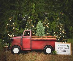 an old red truck with a christmas tree in the bed is parked next to a sign