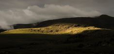 the sun shines through clouds over a grassy hill side with hills in the background