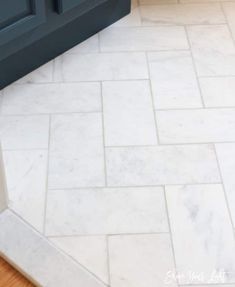 a bathroom with white marble flooring and blue cabinetry in the background, next to a toilet