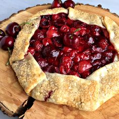 a cherry pie on a wooden plate with cherries around the crust and toppings