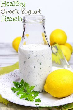 a glass bottle filled with white sauce next to lemons and parsley on a doily