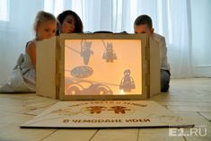 two children sitting on the floor looking at a cardboard box with an image of people inside