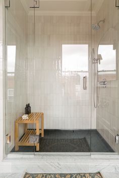 a walk in shower sitting inside of a bathroom next to a wooden table and rug