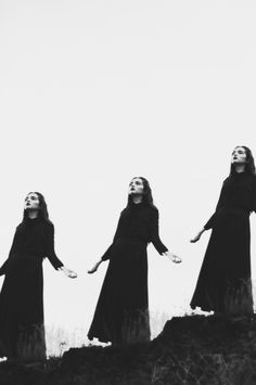 three women in long black dresses standing on top of a hill with their arms outstretched