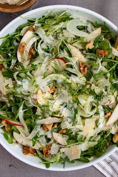 a salad in a white bowl on top of a table next to a fork and napkin