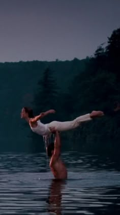 two people are doing acrobatic in the water near some trees and mountains