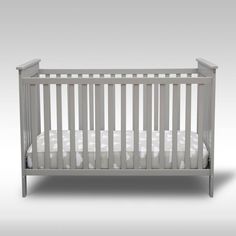 a baby crib with white sheets and pillows on the bottom bed, in front of a gray background