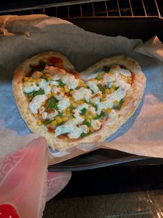 a heart shaped pizza sitting on top of a piece of wax paper in an oven