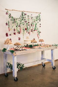 a table topped with cakes and desserts on top of a wooden table covered in greenery