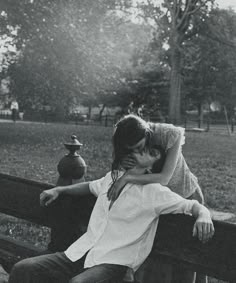 black and white photograph of two people sitting on a bench in a park, one kissing the other