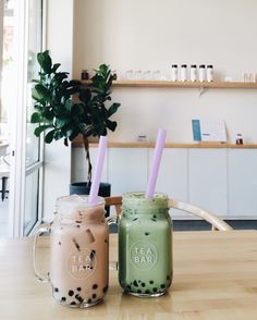 two mason jars filled with drinks sitting on top of a wooden table next to a potted plant