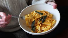 a person holding a bowl of pasta with sage