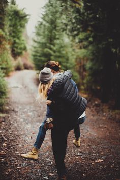 a woman carrying a child on her back in the middle of a road with trees