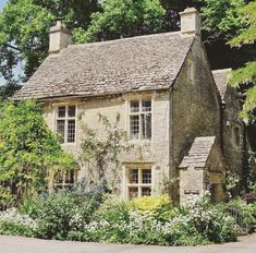 an old stone house surrounded by flowers and trees