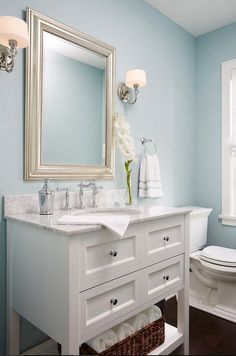 a bathroom with blue walls and white fixtures, including a large mirror over the sink