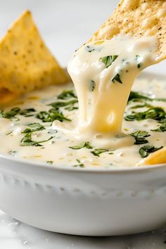 a tortilla chip being dipped into a bowl of cheese and spinach dip