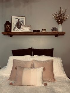 a bed with two pillows and some pictures on the shelf above it in a bedroom