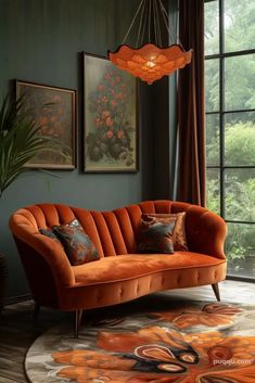 an orange couch sitting in front of a window next to a rug with flowers on it