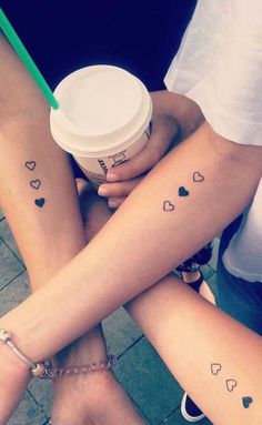 two girls with matching tattoos on their arms holding coffee cups and one has a green straw in her hand