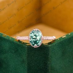 a ring with a green stone in the center on a velvet surface, next to a wooden box