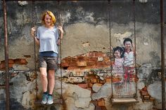 a woman standing on a swing in front of a wall with pictures painted on it