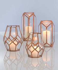 four candles are lit in geometric glass containers