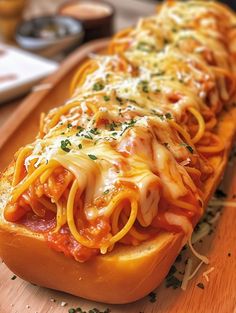 a long hot dog bun with spaghetti and cheese on it sitting on a cutting board