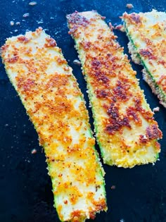 three cooked zucchini sticks on a black surface with seasoning sprinkles