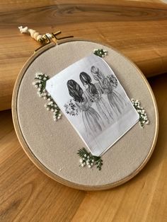 an embroidery project with flowers and pictures on the hoop, sitting on top of a wooden table