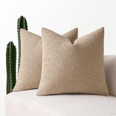 two pillows sitting on top of a white couch next to a green cacti