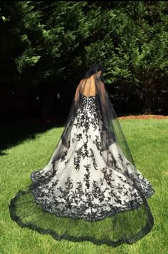 a woman wearing a black and white wedding dress with a veil on her head is standing in the grass