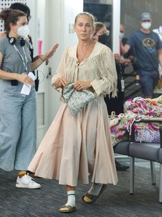 a woman wearing a face mask and carrying a purse walks through an airport terminal with other people in the background