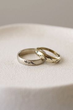 two gold wedding rings sitting on top of a white plate with the word love written on it