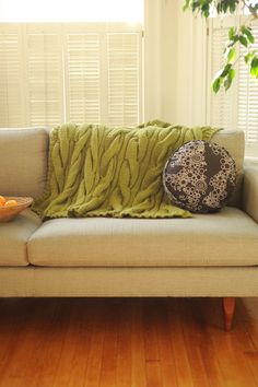 a couch with a green blanket on top of it next to a bowl of fruit