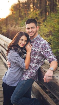 a man and woman standing on a bridge posing for the camera with their arms around each other