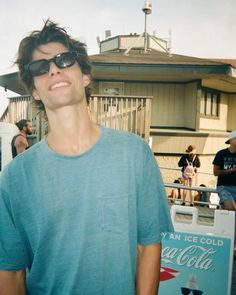 a man wearing sunglasses standing in front of a coca - cola cooler with people looking on