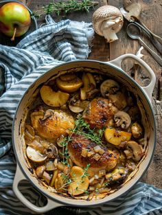 a pot filled with chicken and mushrooms on top of a wooden table next to an apple