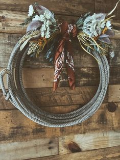 a wreath made out of rope and flowers on top of a wooden wall with a red bow