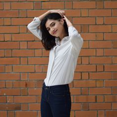 a woman standing in front of a brick wall with her hands on her head and looking at the camera