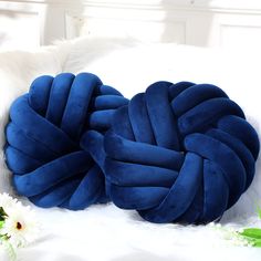 two blue knoted pillows sitting on top of a white bed next to flowers and grass