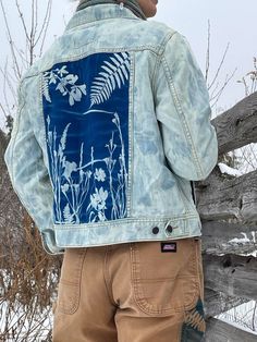 a person standing next to a fence wearing a jean jacket with flowers and leaves on it