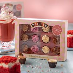 a box of chocolate cupcakes next to a glass of red wine and two cakes