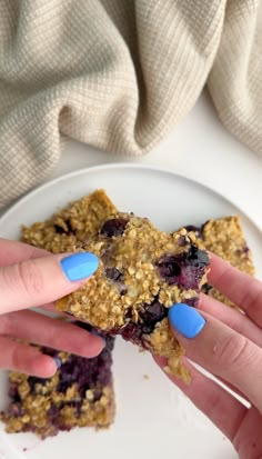 two hands with blue fingernails are holding some food on a plate and another hand is reaching for it