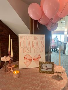 a table with pink balloons and a sign that says wrapping up clara's first year