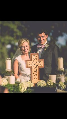 a man and woman standing next to each other in front of a cross with candles