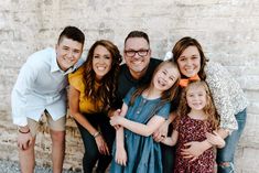 a family poses for a photo in front of a brick wall with their arms around each other