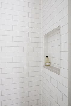 a white tiled shower with a bottle on the shelf in the corner next to it